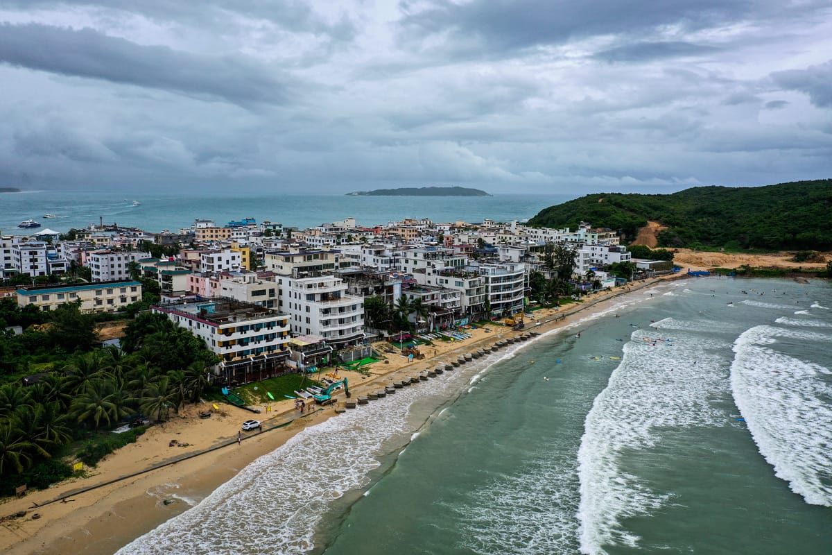 Vista aérea de una playa de Sanya con palmeras, torres turísticas y bahía turquesa en Hainan, China