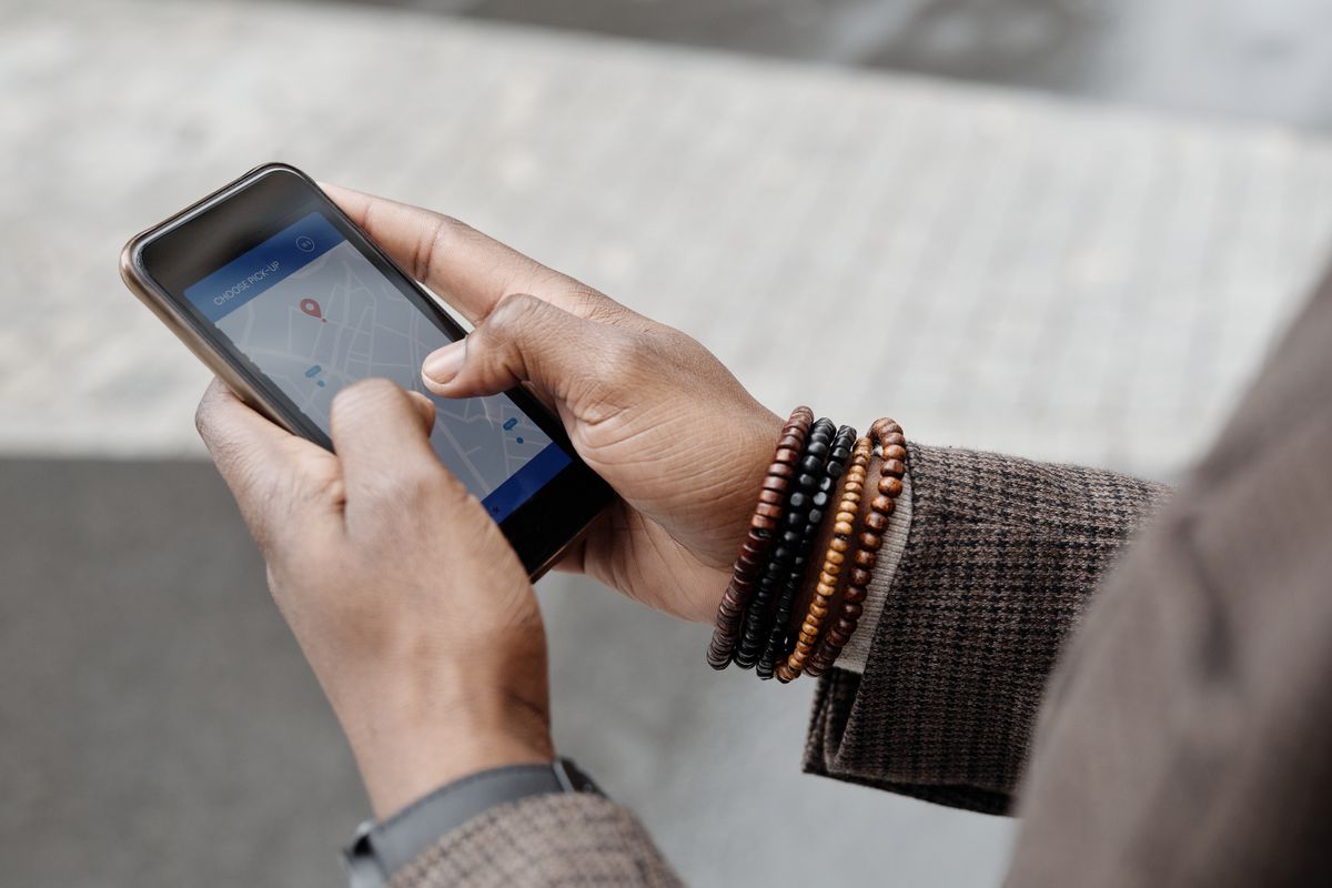 Primer plano de una mano sosteniendo un teléfono con la pantalla de un mapa de una app de transporte y un marcador de recogida