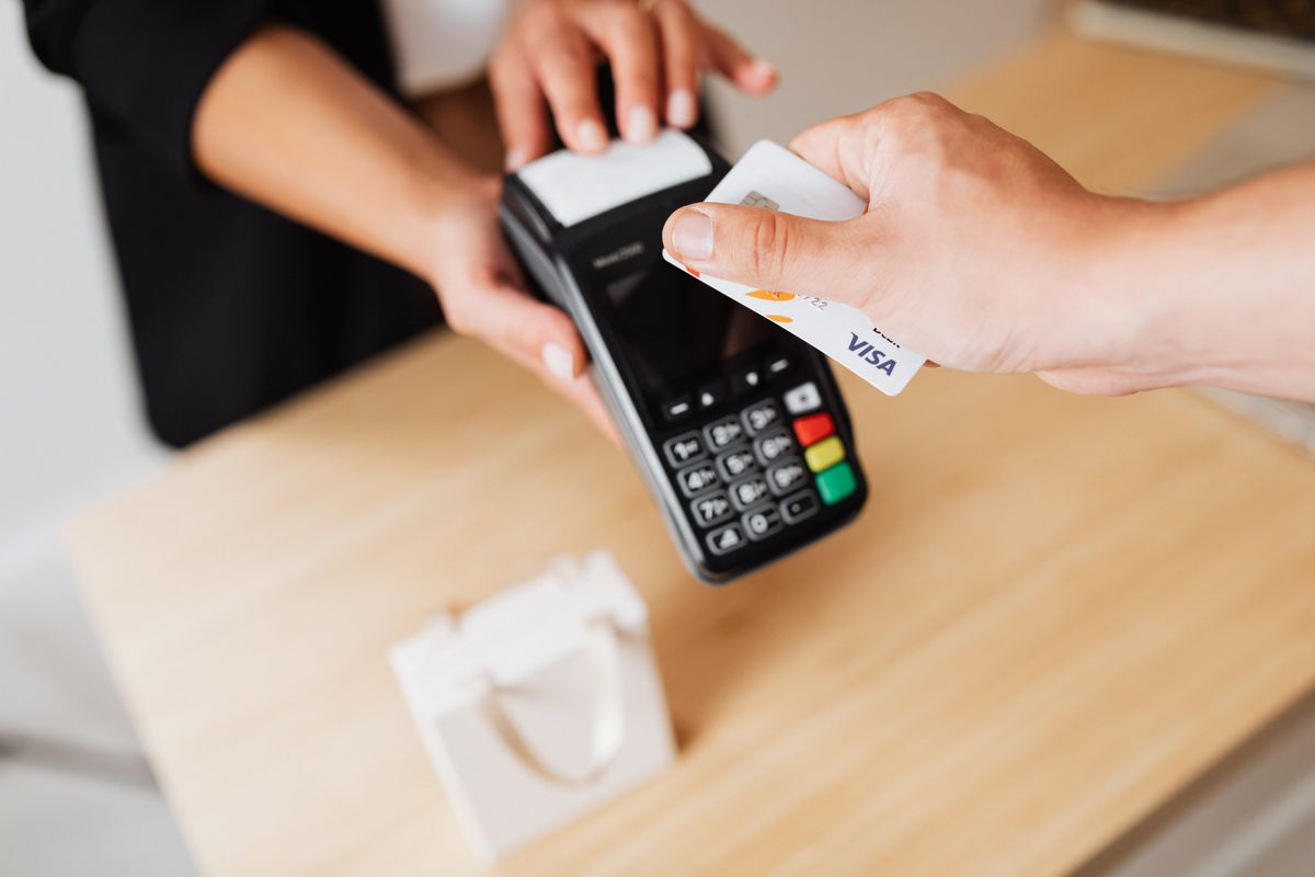 Una mano acercando una tarjeta Visa a un datafono negro sin contacto en el mostrador de una tienda