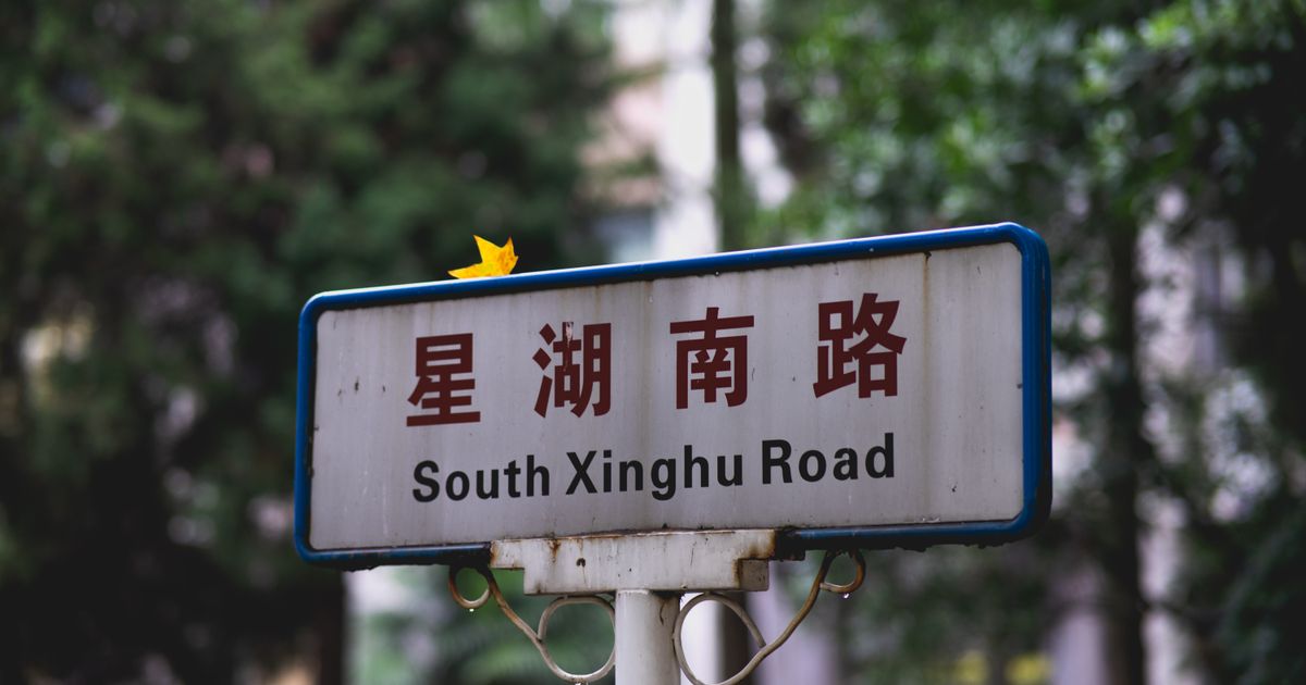 Cartel bilingüe en chino e inglés que dice South Xinghu Road montado en un poste con árboles detrás