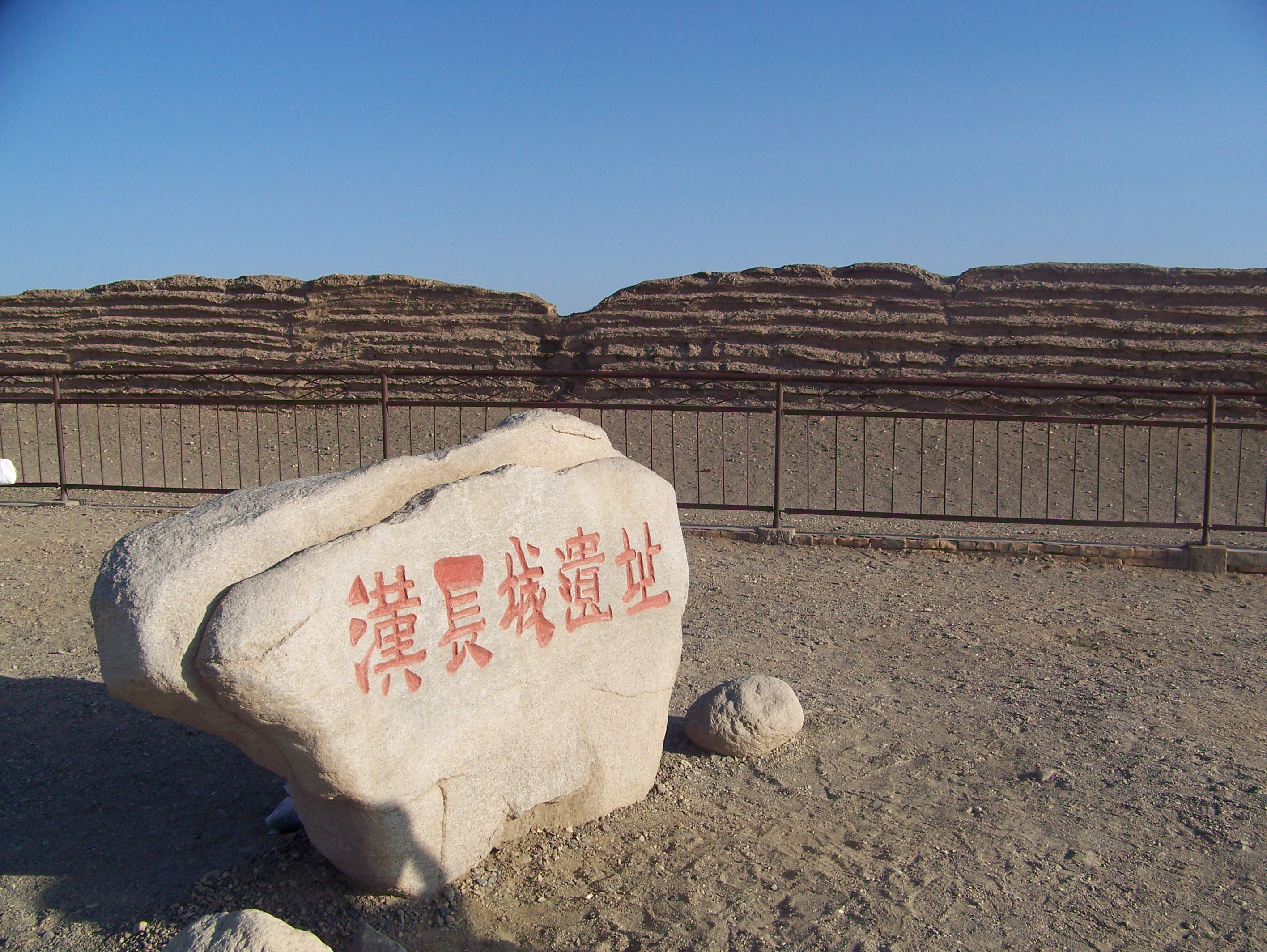 Piedra que marca las "Ruinas de la Gran Muralla Han" ante el muro estratificado