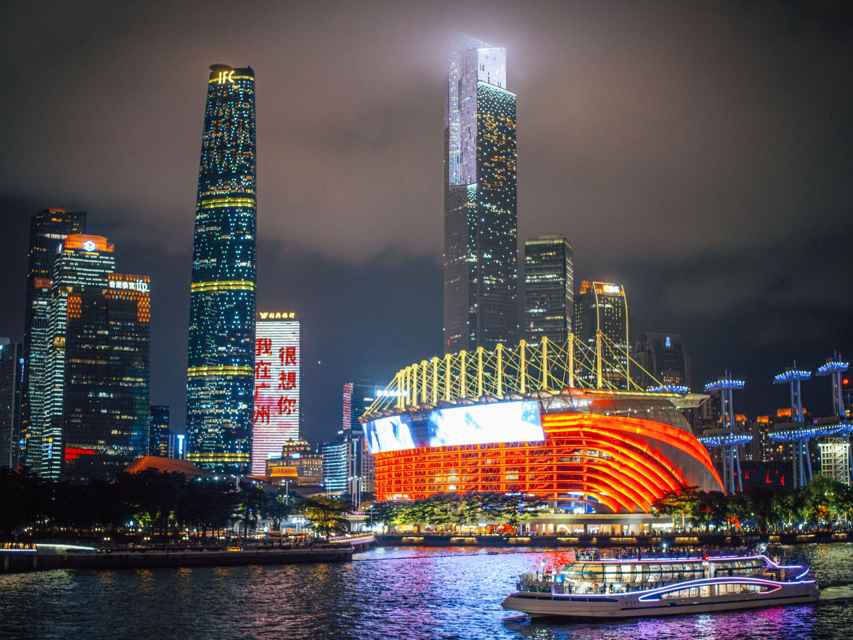 Guangzhou's illuminated riverside skyline at night with a cruise boat on the Pearl River
