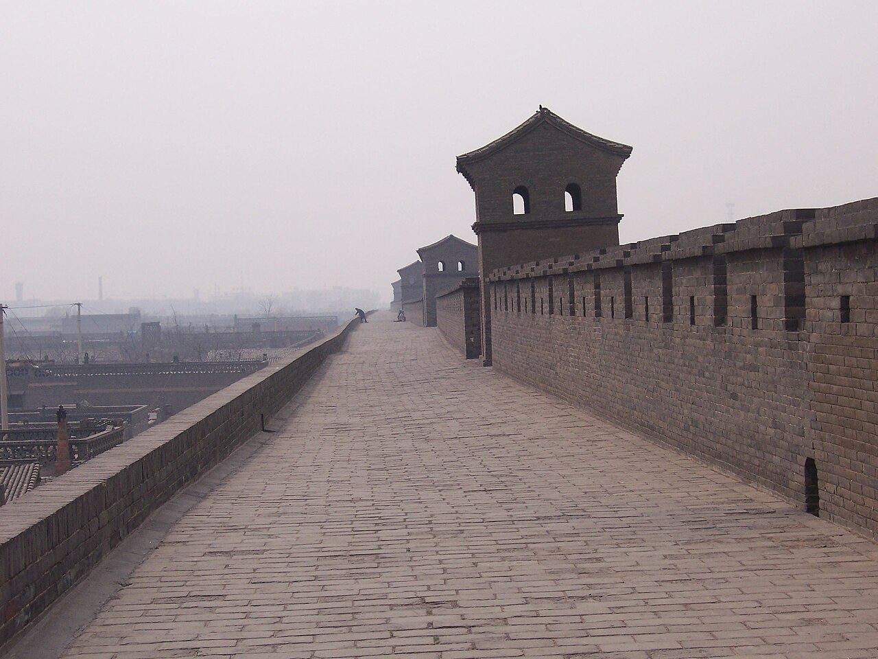 Visitantes paseando por el amplio camino pavimentado sobre la muralla de Pingyao junto a una torre de vigilancia
