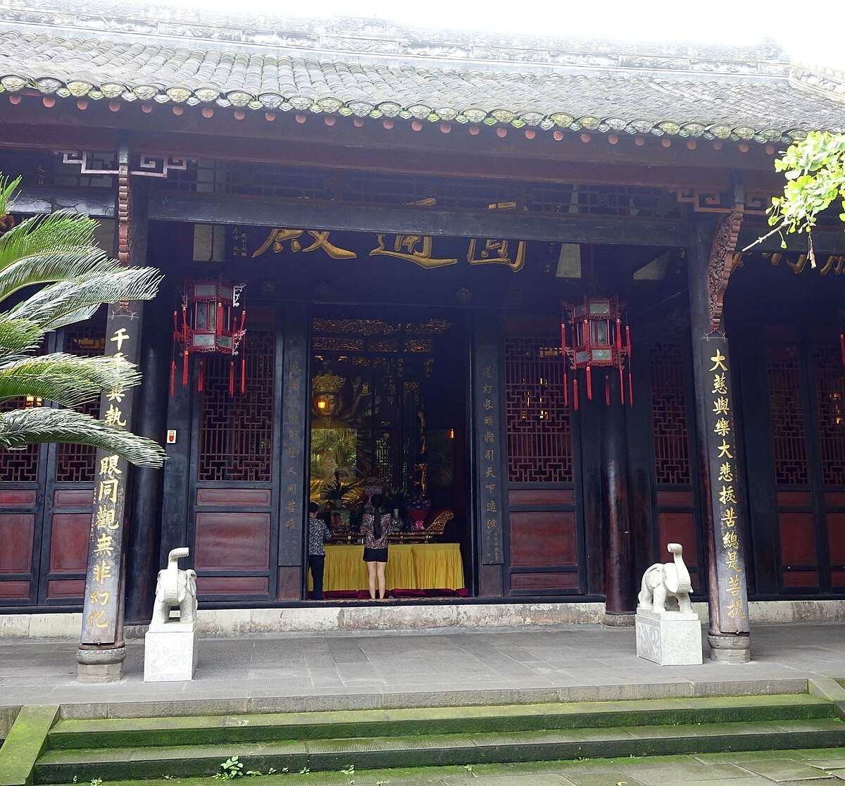 Sala del Monasterio de Wenshu enmarcada por palmeras y leones de piedra