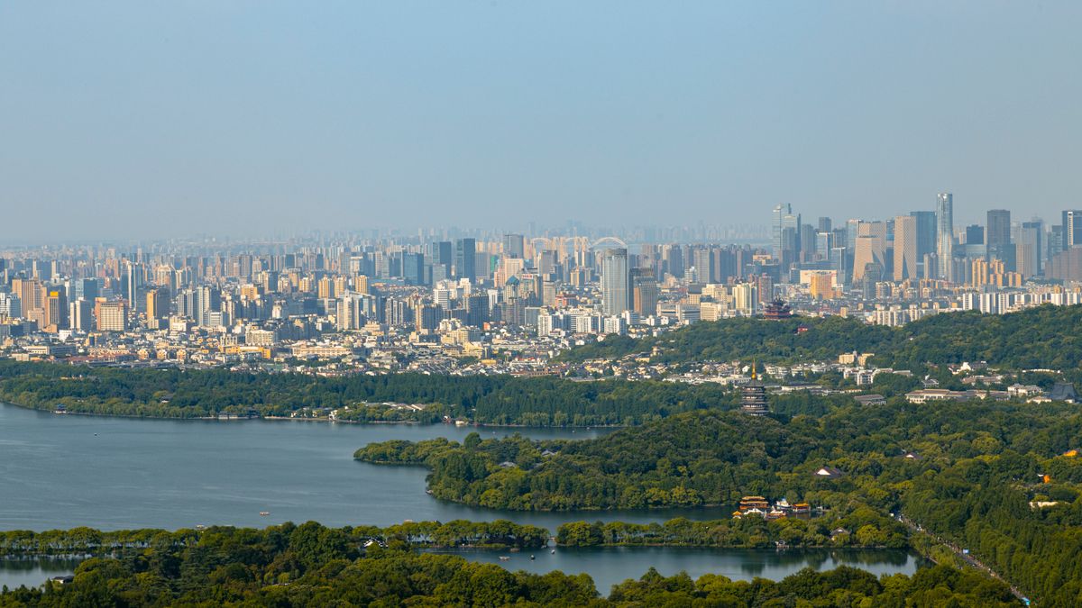Aerial view of Hangzhou's skyline rising behind West Lake, with the city's commercial district beyond the shoreline