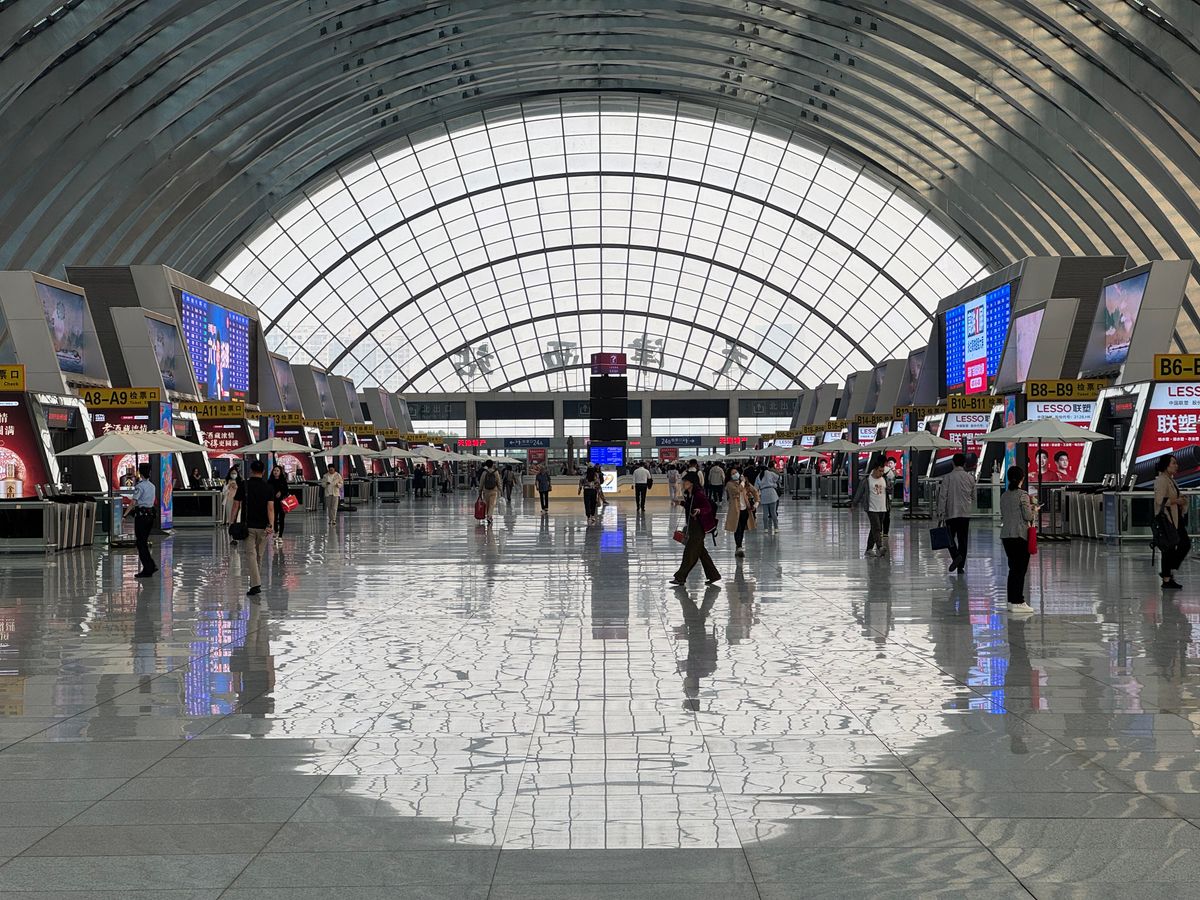 Interior of a modern Chongqing transit hub with departure boards and travelers crossing a bright, glass-roofed hall