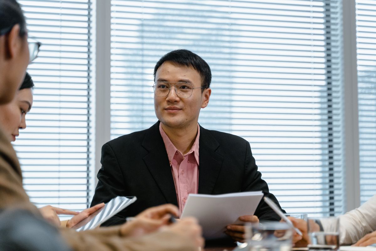 Asian businessman in a suit sitting at the head of a meeting table with colleagues