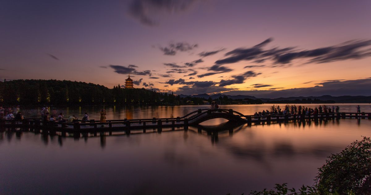 Sunset over West Lake with the silhouette of Leifeng Pagoda and a stone bridge