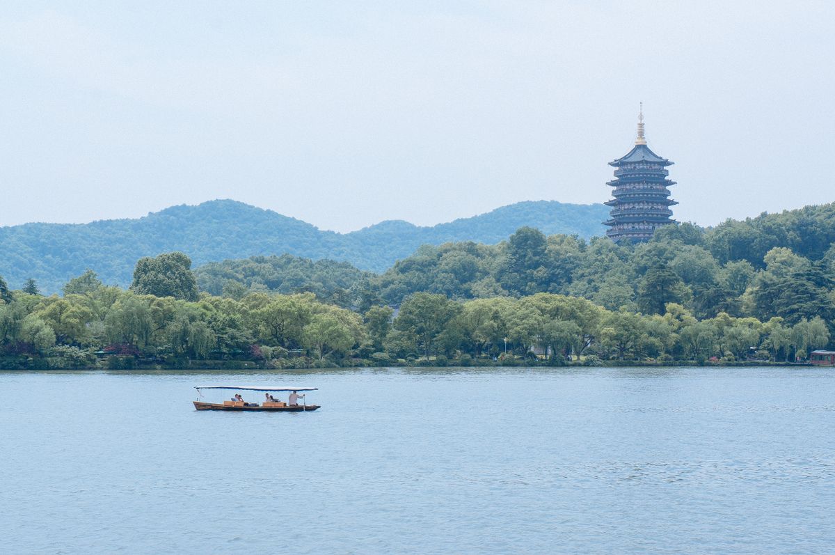 Traditional wooden boat on West Lake with Leifeng Pagoda visible across the water