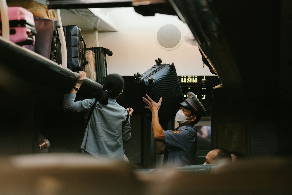 Train conductor and passenger loading a large suitcase onto an overhead luggage rack