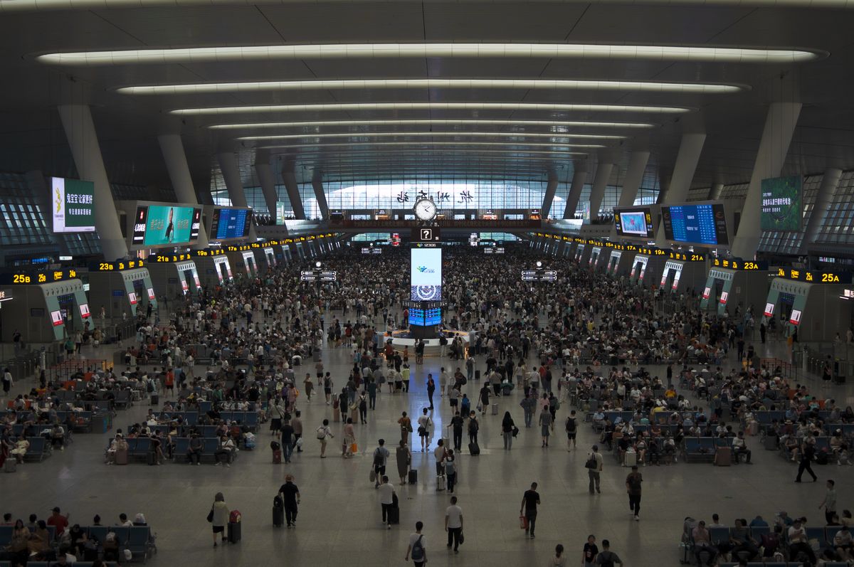 Wide view of a crowded China railway station waiting hall with departure boards