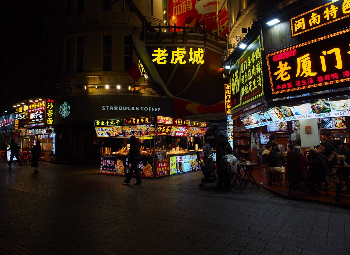 Neon-lit night street food market in China with Chinese signage and food stalls