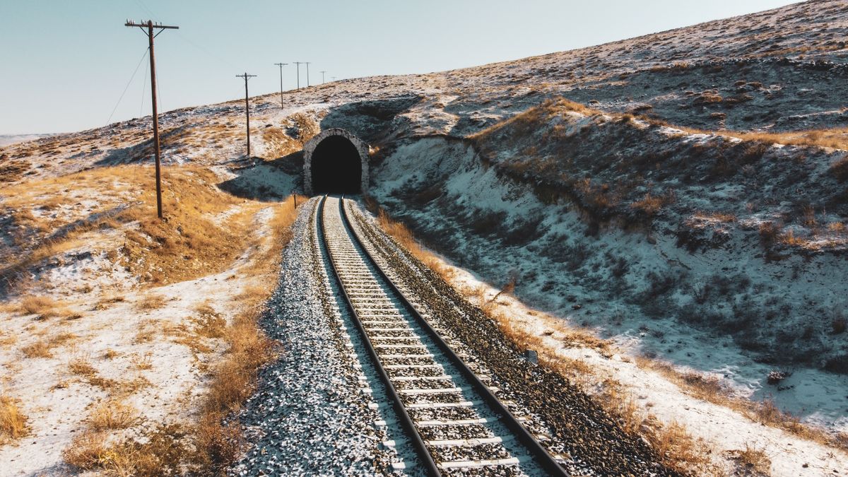 Railway tracks leading into a mountain tunnel in a hilly landscape