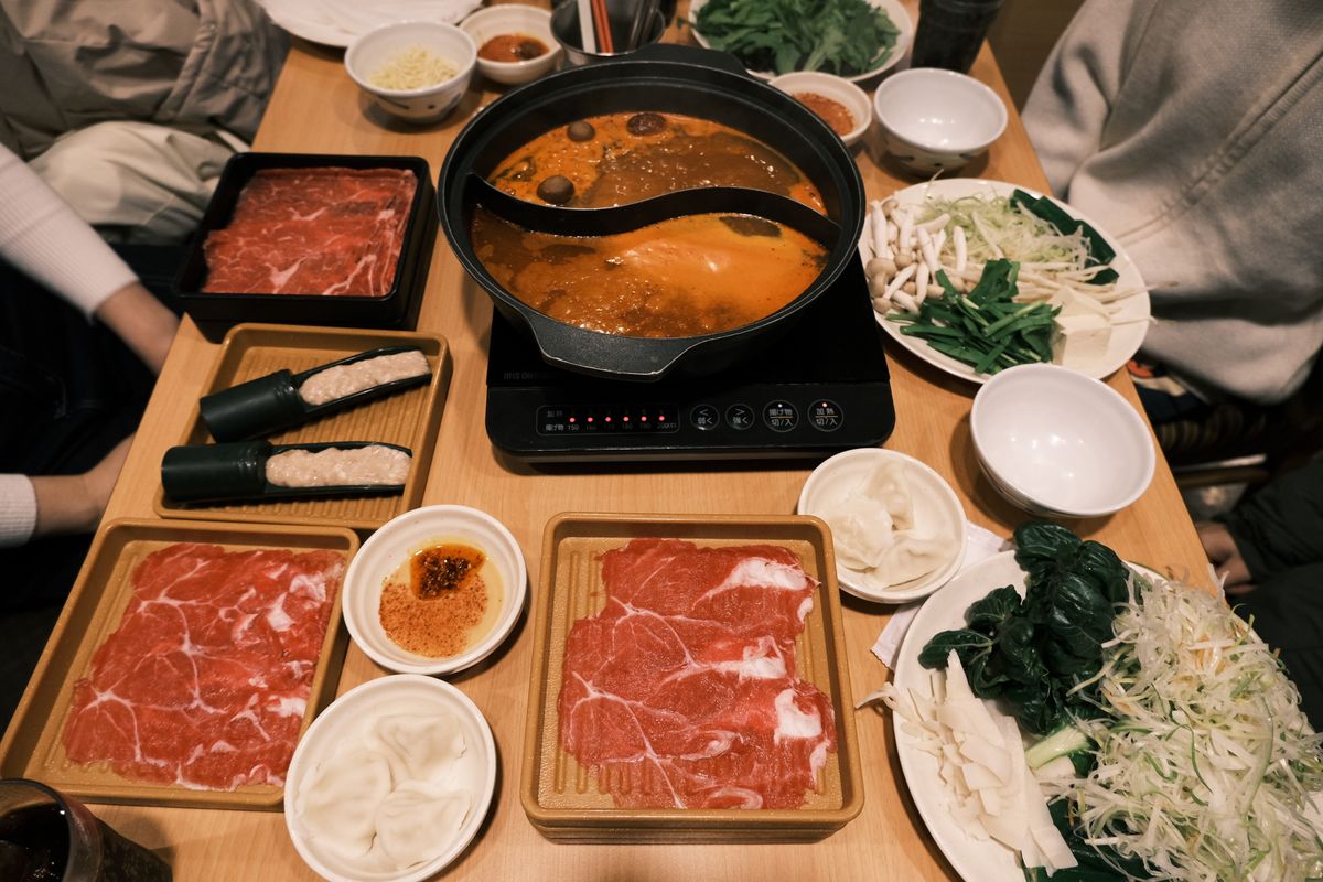 Bowl of Sichuan-style hot pot broth with sliced lotus root and meat ready to cook