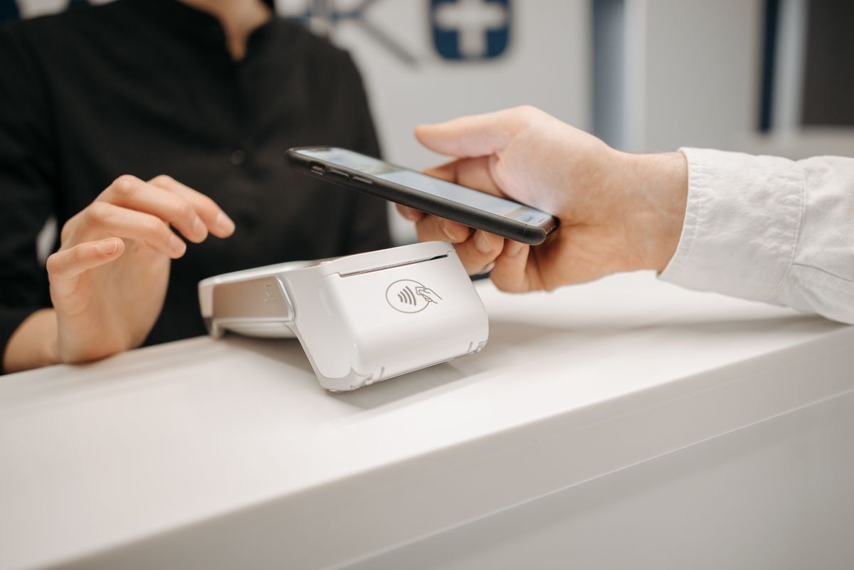 Person tapping a smartphone against a payment terminal at a retail counter