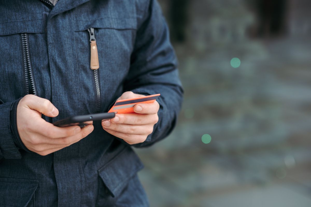 Man outdoors holding a smartphone and a bank card, about to link the card while traveling