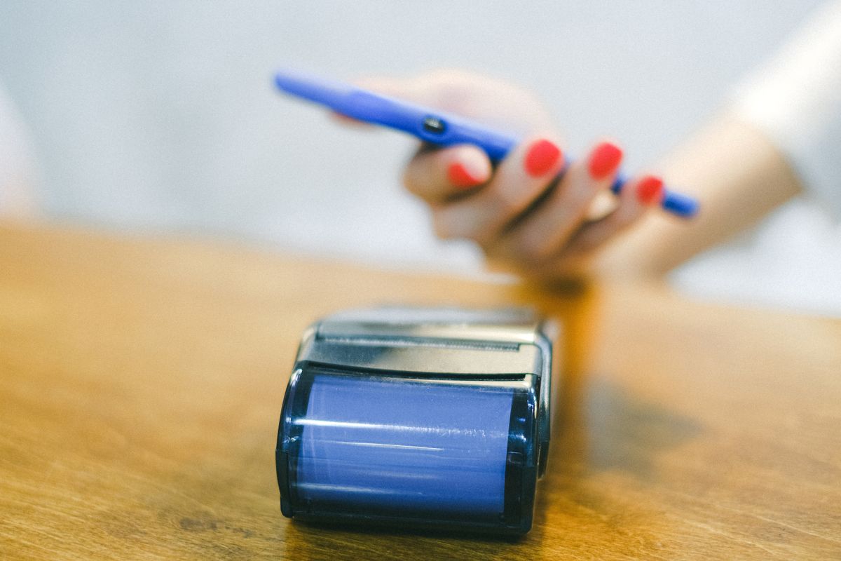 Close-up of a blue payment terminal with a smartphone being tapped to pay