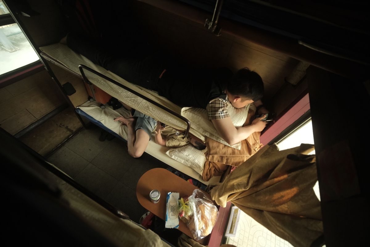 Interior of a Chinese sleeper train compartment with bunks and a passenger resting