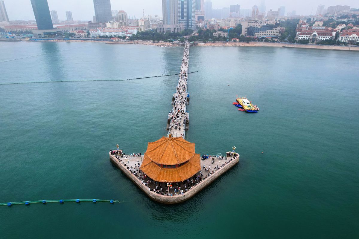 Aerial view of Zhanqiao Pier extending into the sea with Qingdao's skyline behind it
