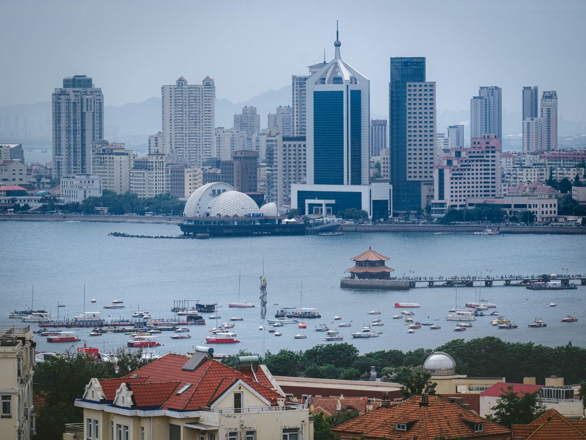 Red-roofed old town buildings with Qingdao's modern skyline and bay in the background