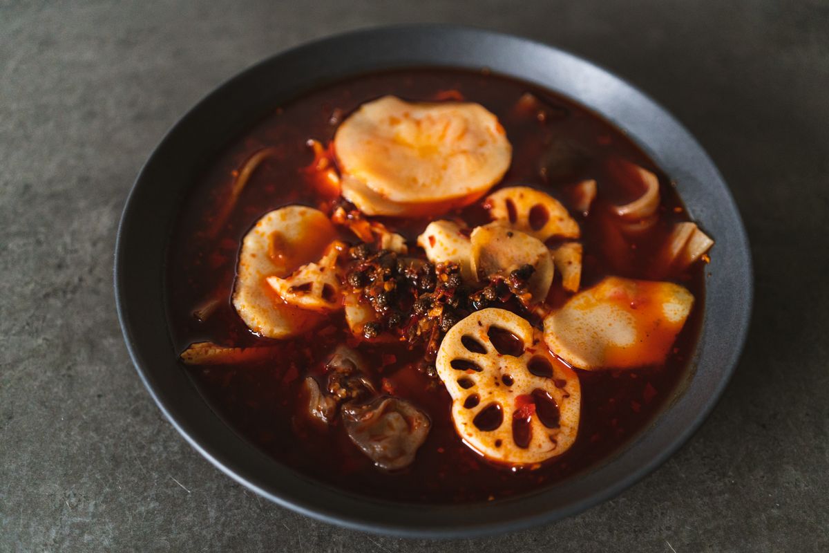 A bowl of Sichuan hotpot with lotus root, mushrooms and chili oil
