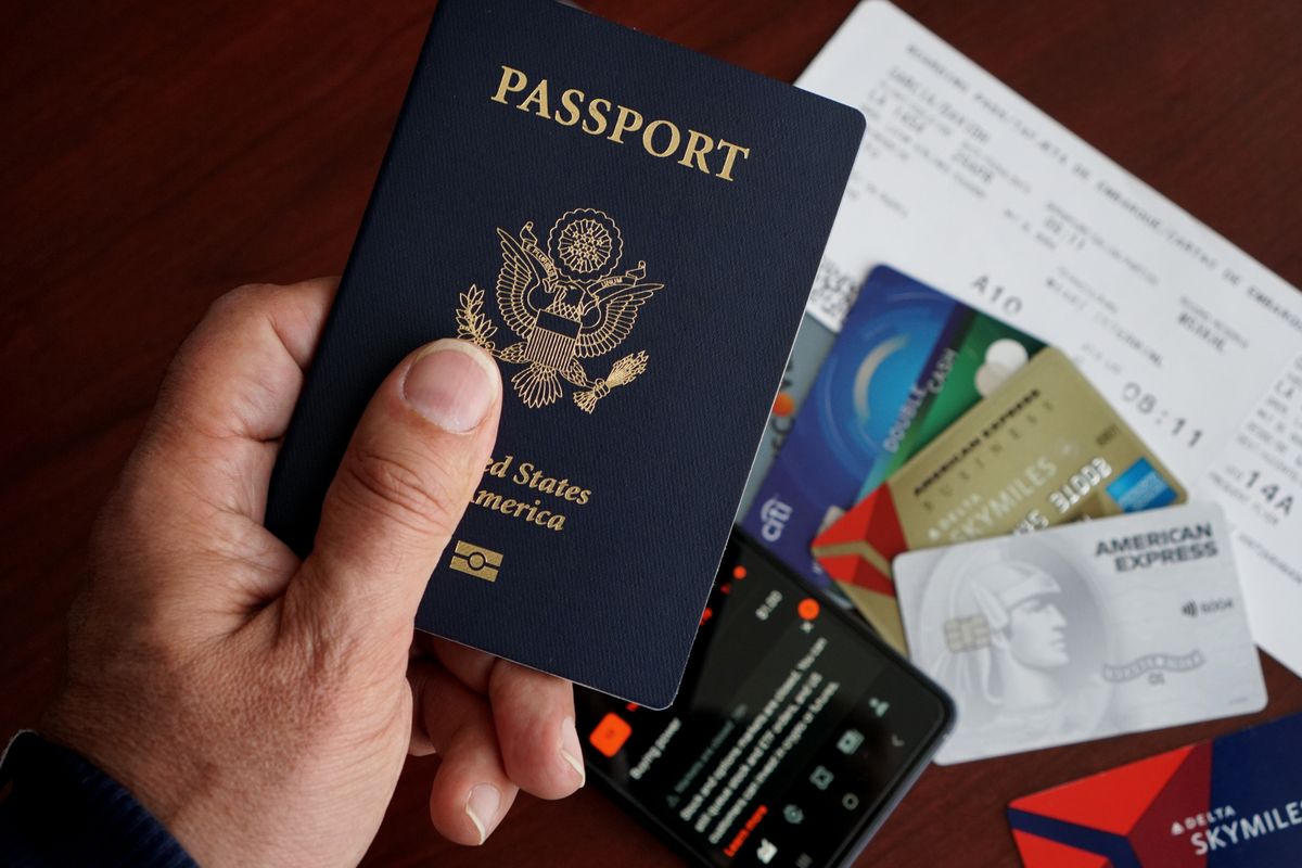 Mano sosteniendo un pasaporte estadounidense con tarjetas de crédito y una tarjeta de embarque