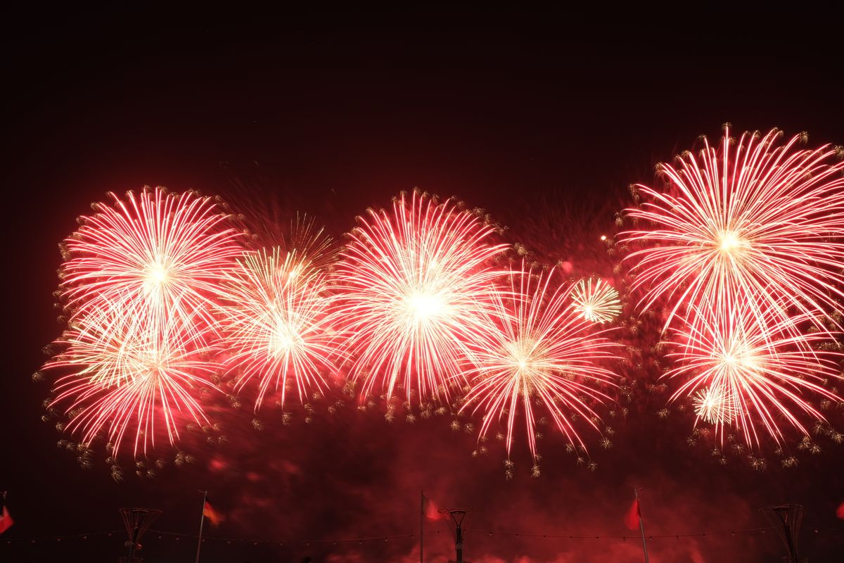Fireworks explode in red and gold against a dark night sky during a festival celebration