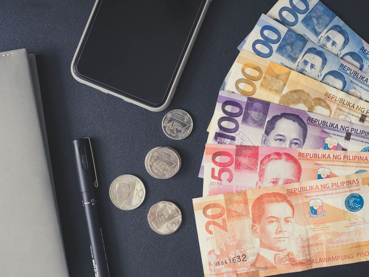 Philippine peso banknotes and coins fanned out next to a phone and notebook