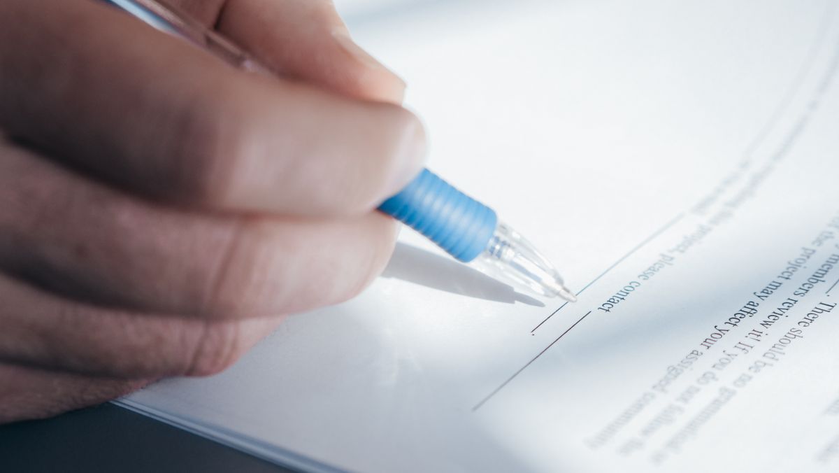Close-up of a hand signing a printed application document