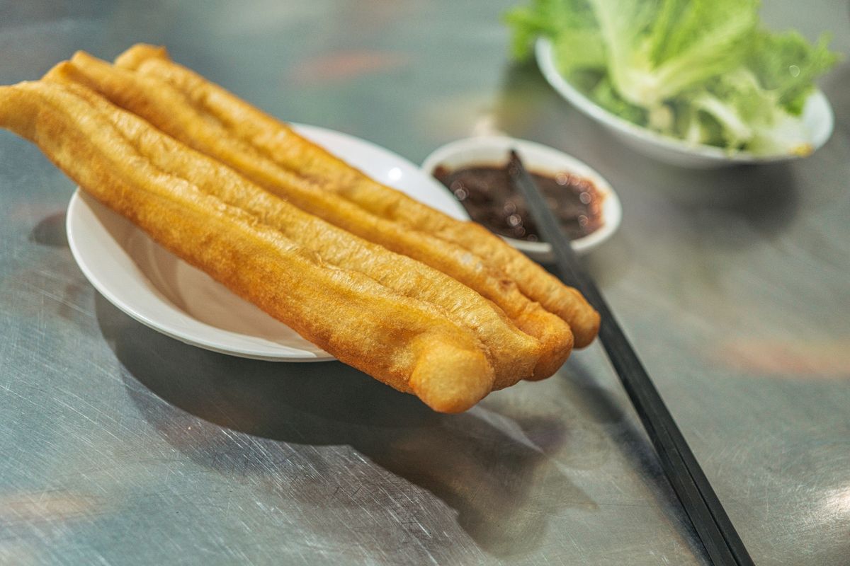 Golden fried youtiao dough sticks on a plate with dipping sauce and greens