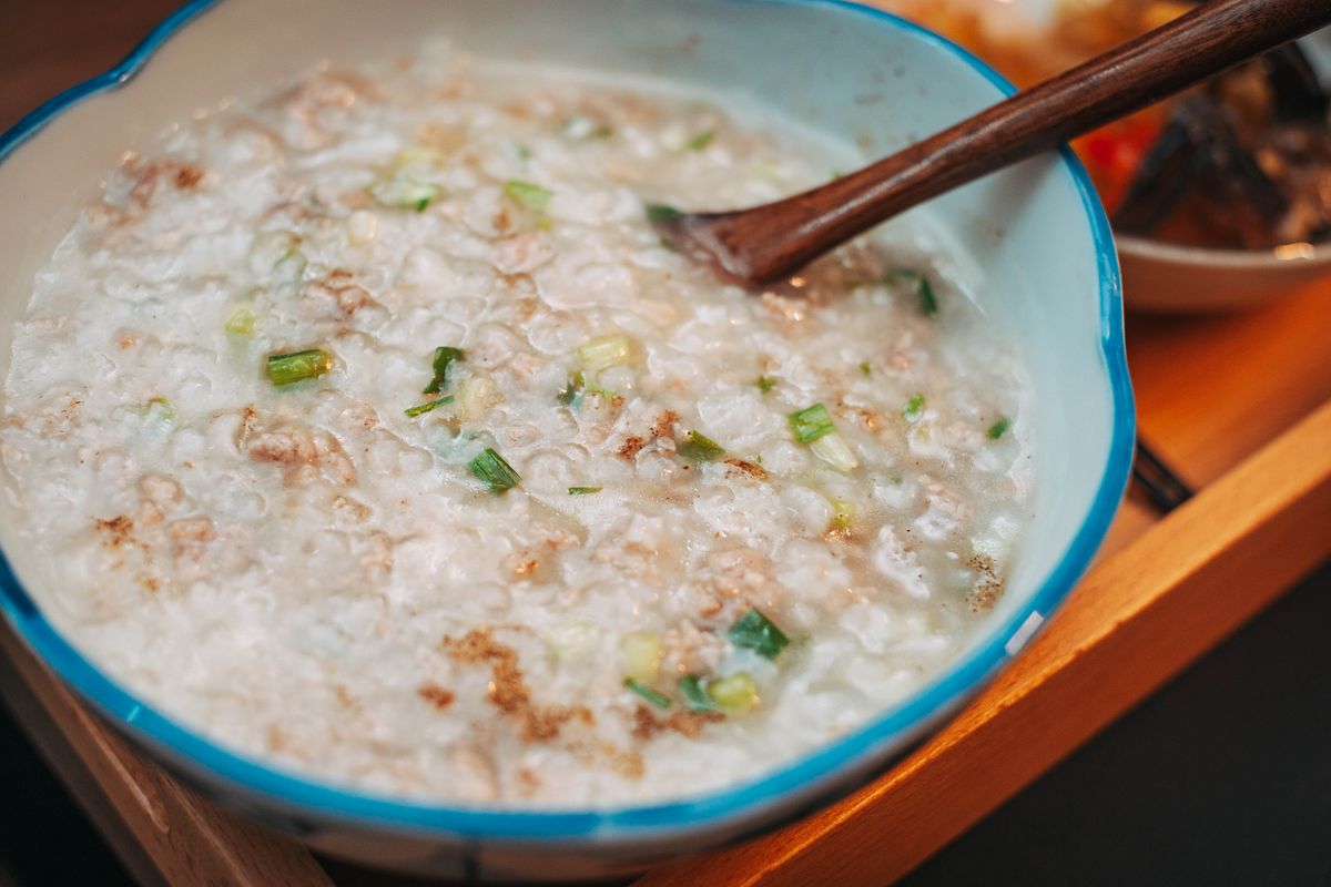 A bowl of Chinese rice congee with pork and scallions and a wooden spoon