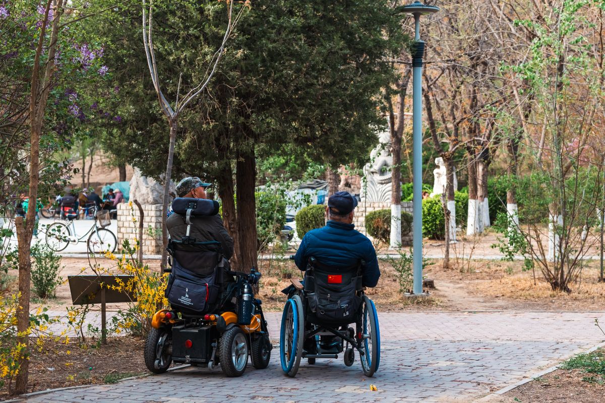 Wheelchair users on a paved path in a Chinese park