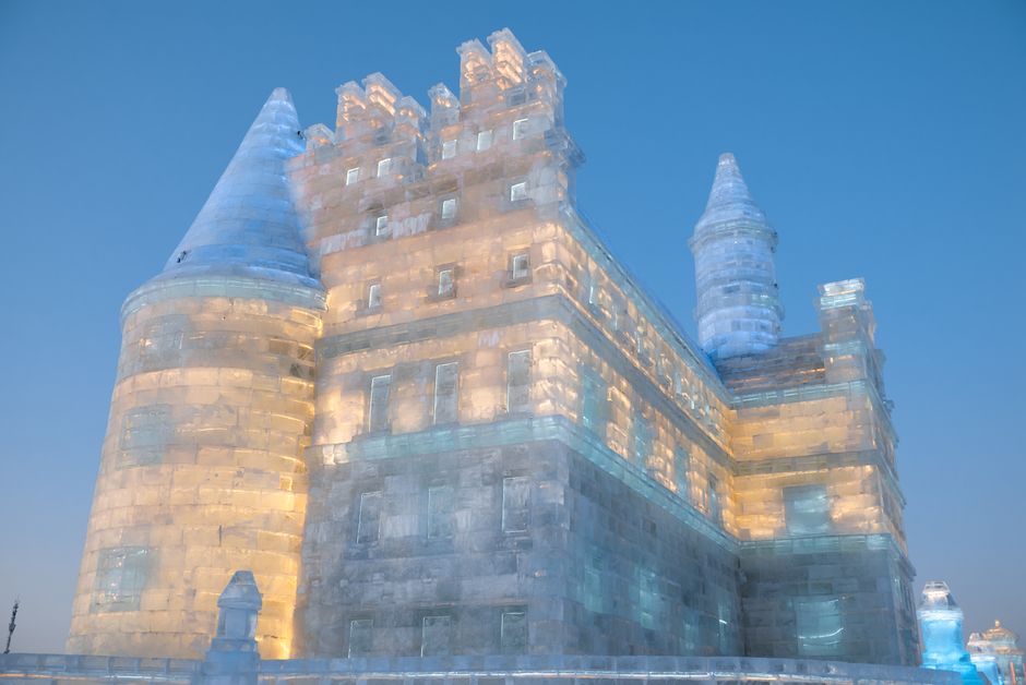 A stunning ice castle glowing with warm lights against a clear evening sky, showcasing winter's artistic beauty.