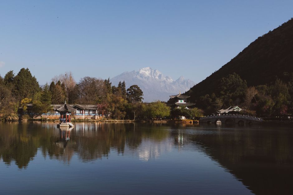 A tranquil lakeside view with traditional architecture and mountains in the background.