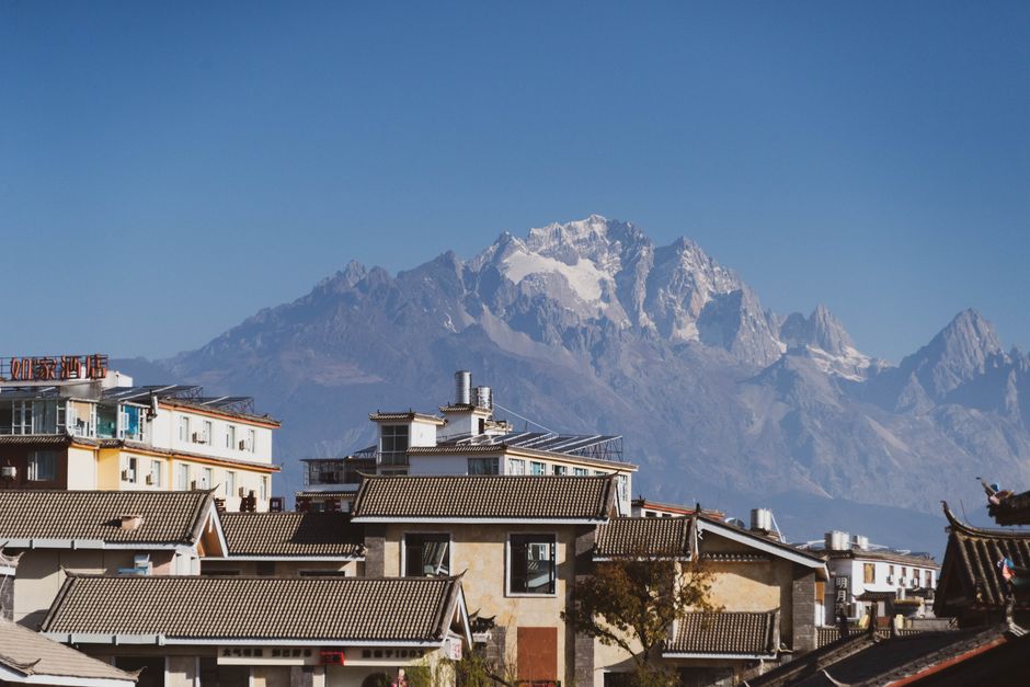 Charming town with traditional roofs against majestic snow-capped mountains on a clear, sunny day.
