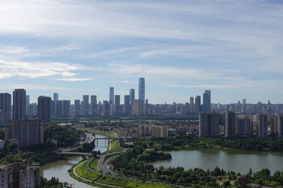 Aerial view of a modern cityscape with towering skyscrapers and a scenic river under a clear blue sky.