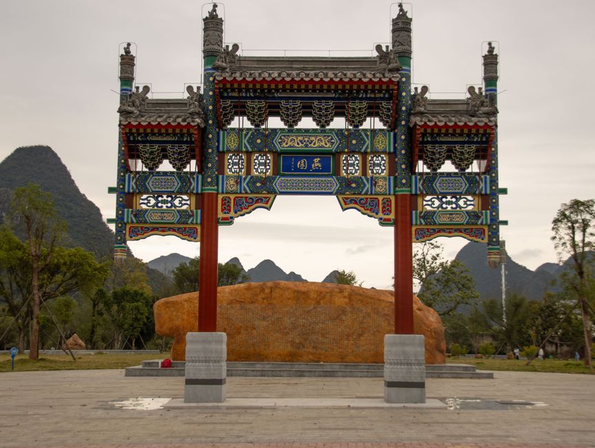 A traditional Chinese archway stands gracefully in a scenic park, set against distant hills.