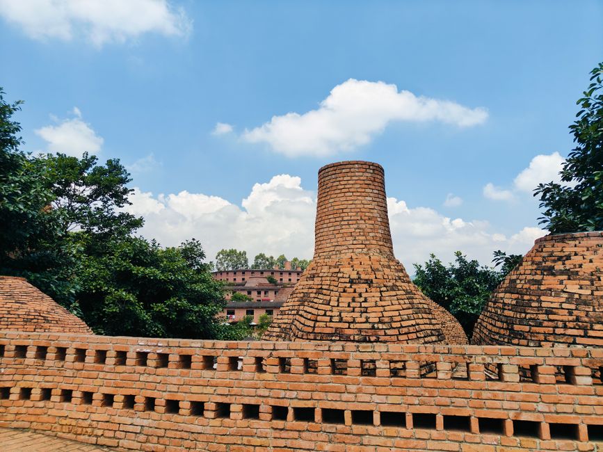 Traditional brick kilns under a clear blue sky surrounded by lush greenery.