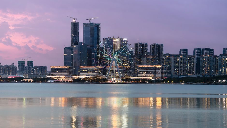 Stunning cityscape featuring a brightly illuminated Ferris wheel at sunset by the waterfront.